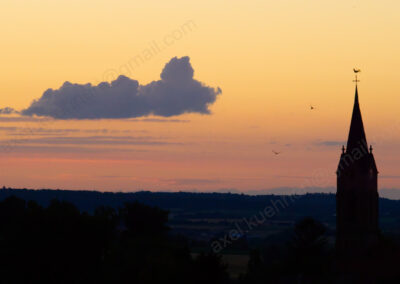 Am pastellfarbenen Abendhimmel strebt eine Drachenwolke dem Kirchturm von Mühlbach zu.