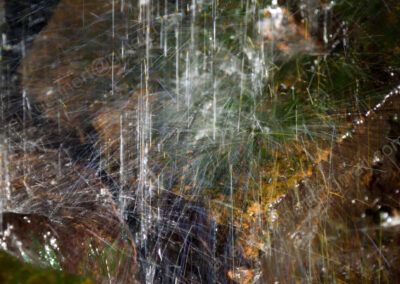 Fallende, und spritzende Tropfen eines kleinen Wasserfalls bilden infolge der Lichtstreuung bunte Fäden.