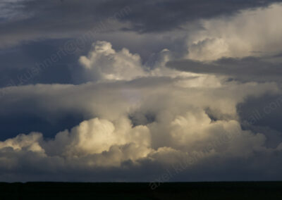 Hinter horizontalen Wolkenbändern türmen sich mit Licht und Schatten riesige Haufenwolken wie zu einem Wolkenpalast auf.